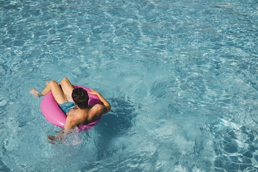 Jeune homme sur une bouée gonflable dans une piscine bleu clair