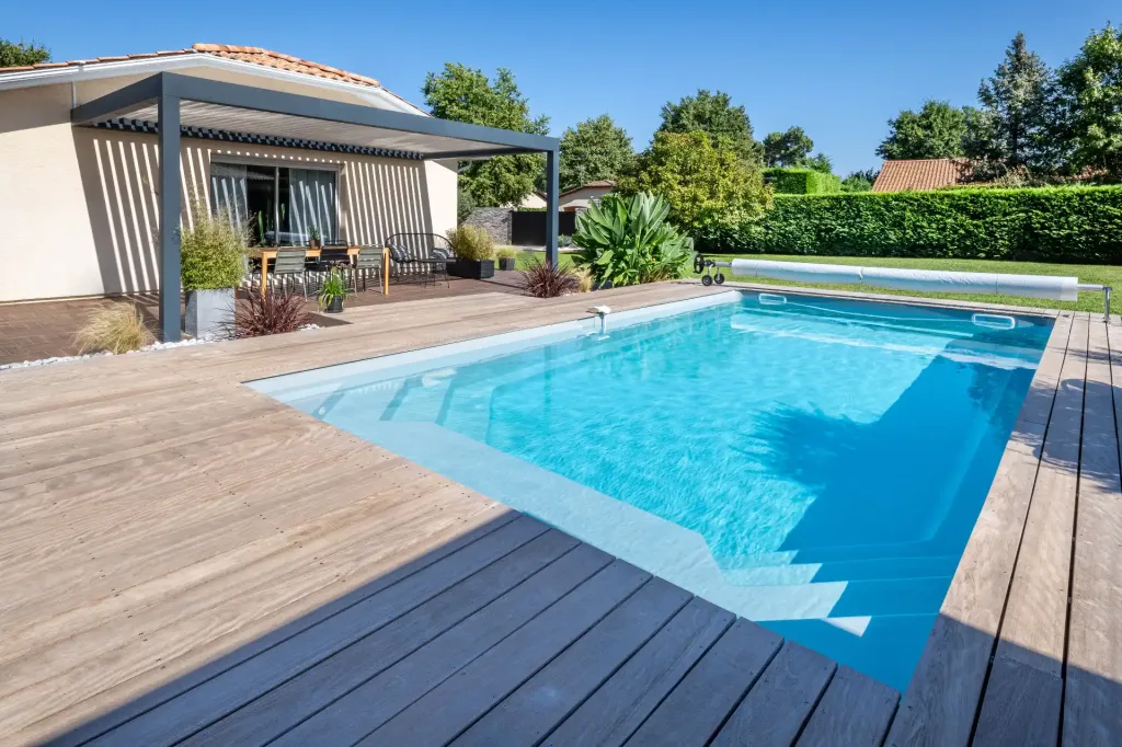 Piscine rectangulaire turquoise avec terrasse en bois et pergola moderne, vue latérale ensoleillée