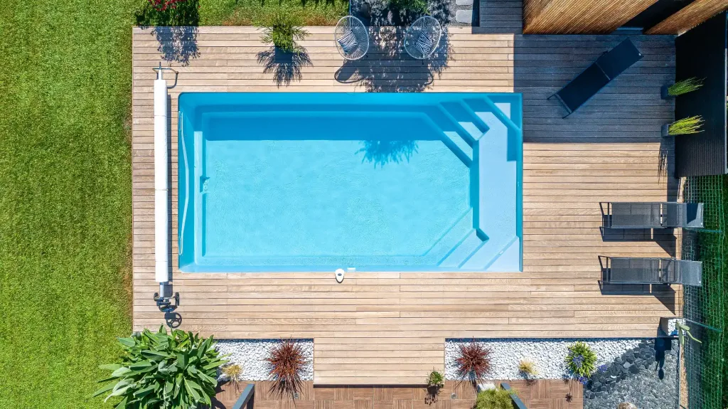 Piscine turquoise entourée de transats bleus, terrasse carrelée et jardin paysager avec pelouse synthétique