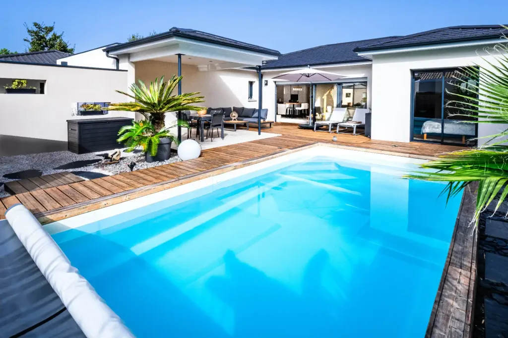 Piscine rectangulaire turquoise avec escalier intégré sur terrasse en bois et mur en pierre