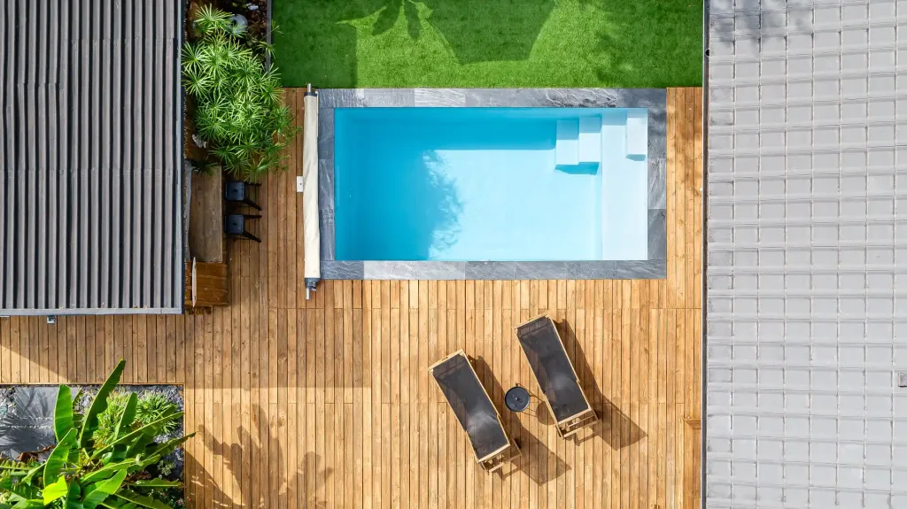 Vue aérienne d’une piscine rectangulaire turquoise avec escalier sur terrasse en bois et gazon