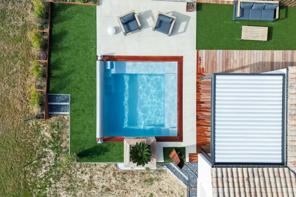 Piscine carrée moderne avec volet roulant dans un jardin contemporain avec terrasse en béton, salon de jardin et deck en bois