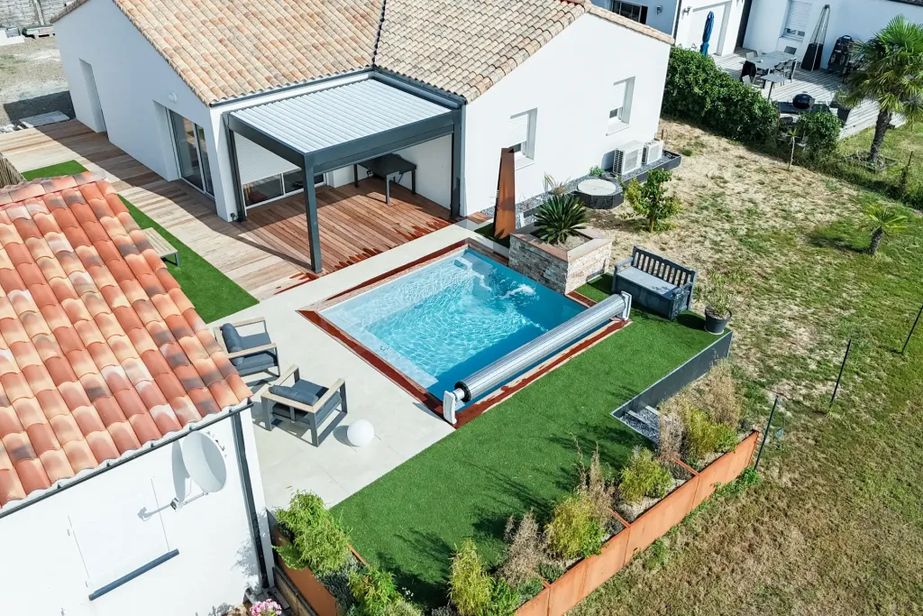 Vue aérienne d'une maison moderne avec piscine rectangulaire, terrasse en bois, pergola, et jardin paysager