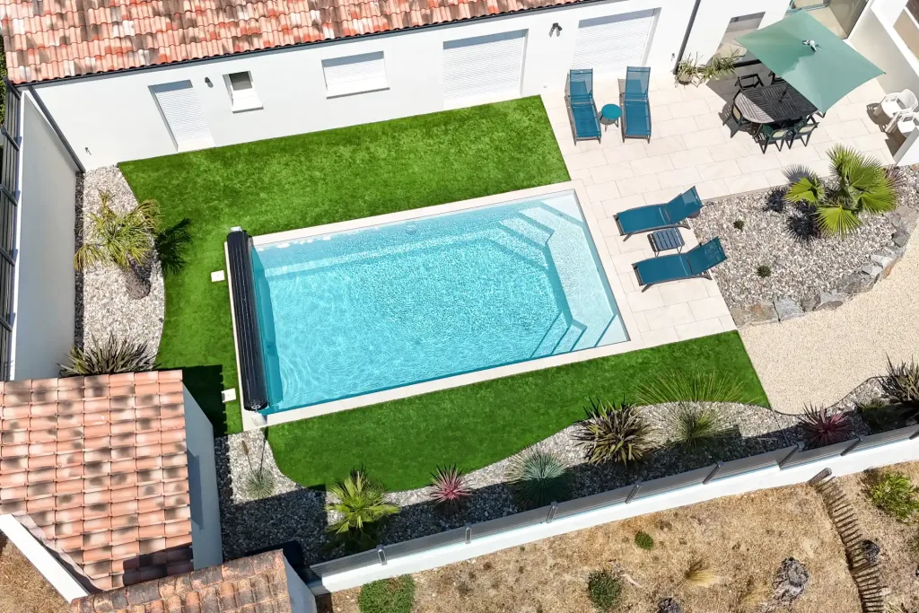 Vue aérienne d'une piscine rectangulaire bleue sur une grande terrasse en bois, avec transats et espace détente