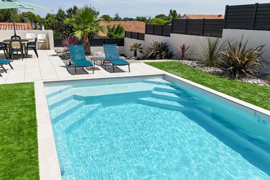Piscine rectangulaire dans un jardin avec terrasse en pierre claire, transats roses et grand parasol, vue aérienne