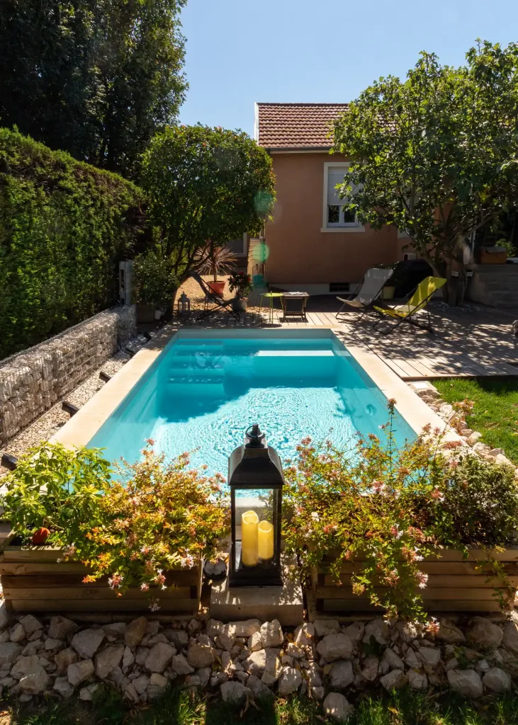 Piscine rectangulaire turquoise entourée d’une haie végétale dense et terrasse en bois
