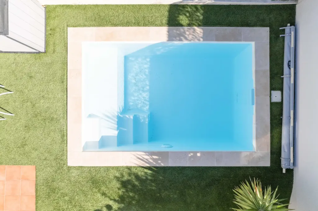 Vue aérienne d’une mini-piscine rectangulaire blanche avec escalier sur gazon synthétique
