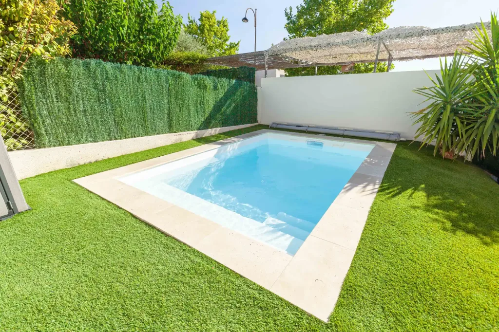 Mini-piscine rectangulaire turquoise entourée de pelouse artificielle et haie végétale