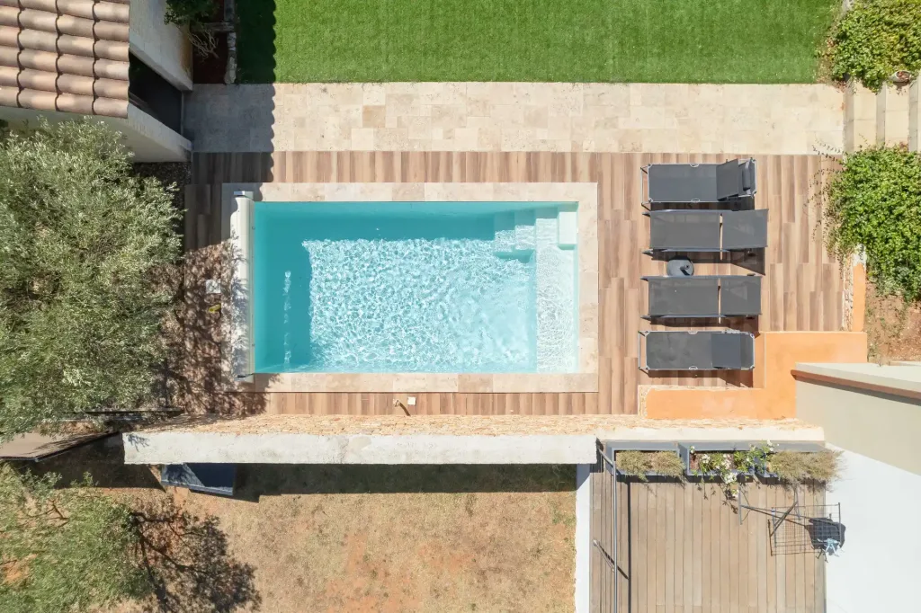 Vue aérienne d’une piscine rectangulaire turquoise avec escalier sur terrasse en bois et pierre