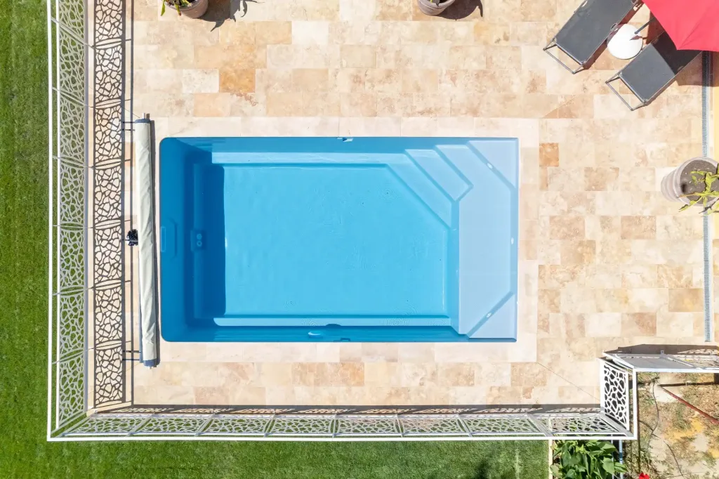 Vue aérienne d’une piscine rectangulaire bleue avec escalier sur terrasse en travertin beige